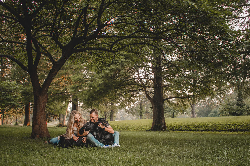 Couple with dogs sitting in grass under trees in Francis Park STL.