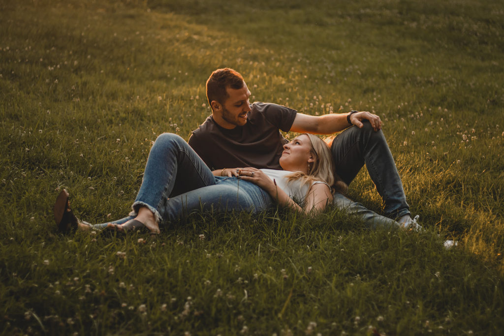 Young woman casually laying on her fiance's lap surrounded by a field dandelions.