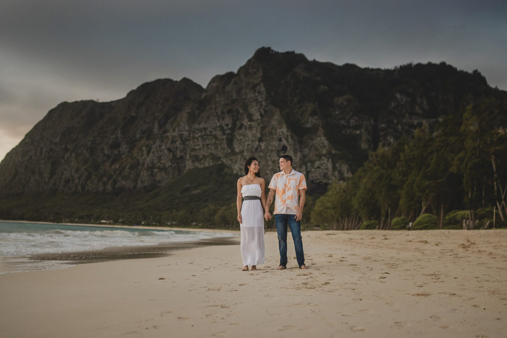 Couple standing on the beach with a mountain in the background in Hawaii.