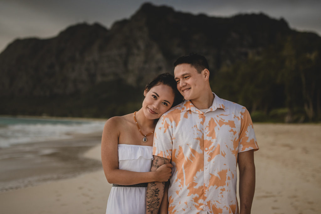 Couple standing on the beach holding arms in Hawaii.
