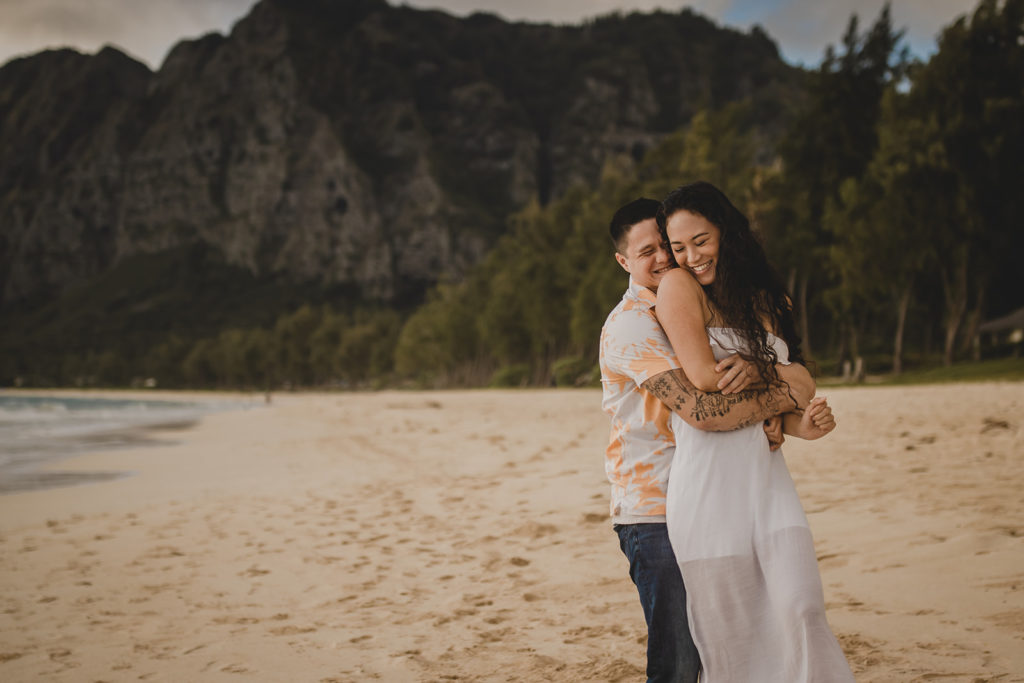 Couple embracing on the beach with a mossy green cliff in the background.