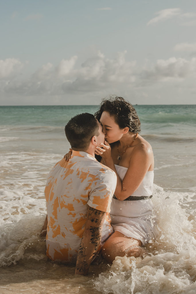 Young engaged couple in surf on the beach kissing.