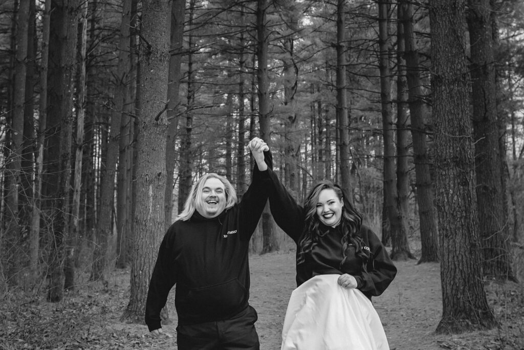 black and white shot of bride and groom smiling towards the camer with hands together held high in celebration