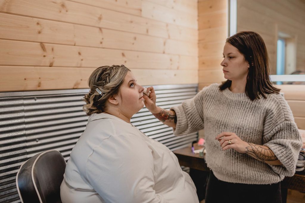 Bride in robe getting makeup applied before wedding ceremony