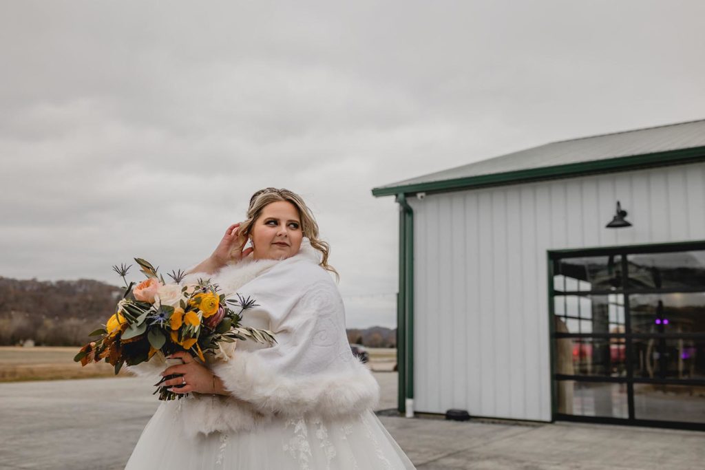 Bride poses in front of her wedding venue holding flowers