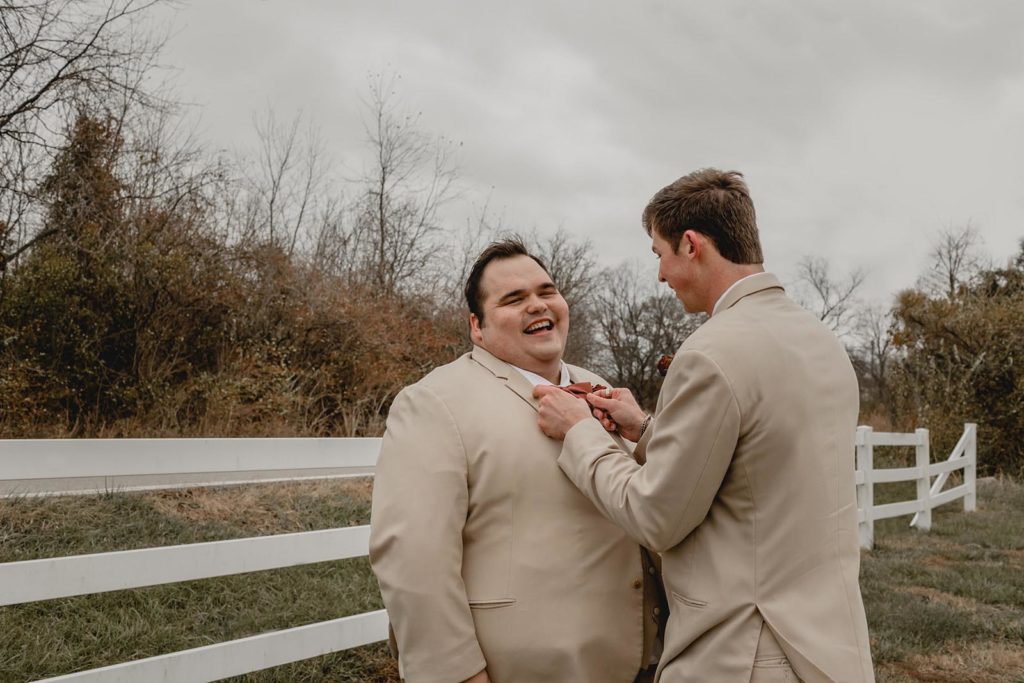 Best man helps groom put on his bowtie on wedding day.