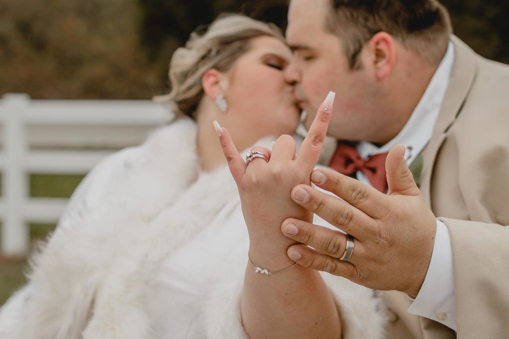 Bride and groom showing off their rings to the camera while kissing