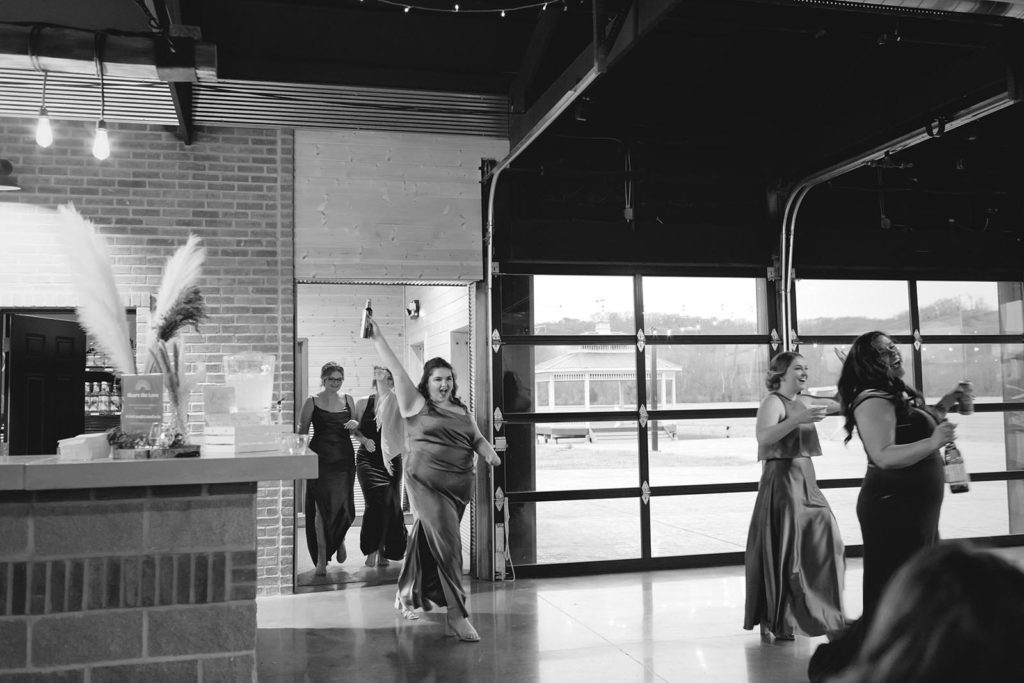 Bridesmaid celebrating and walking into wedding reception with arms in the air
