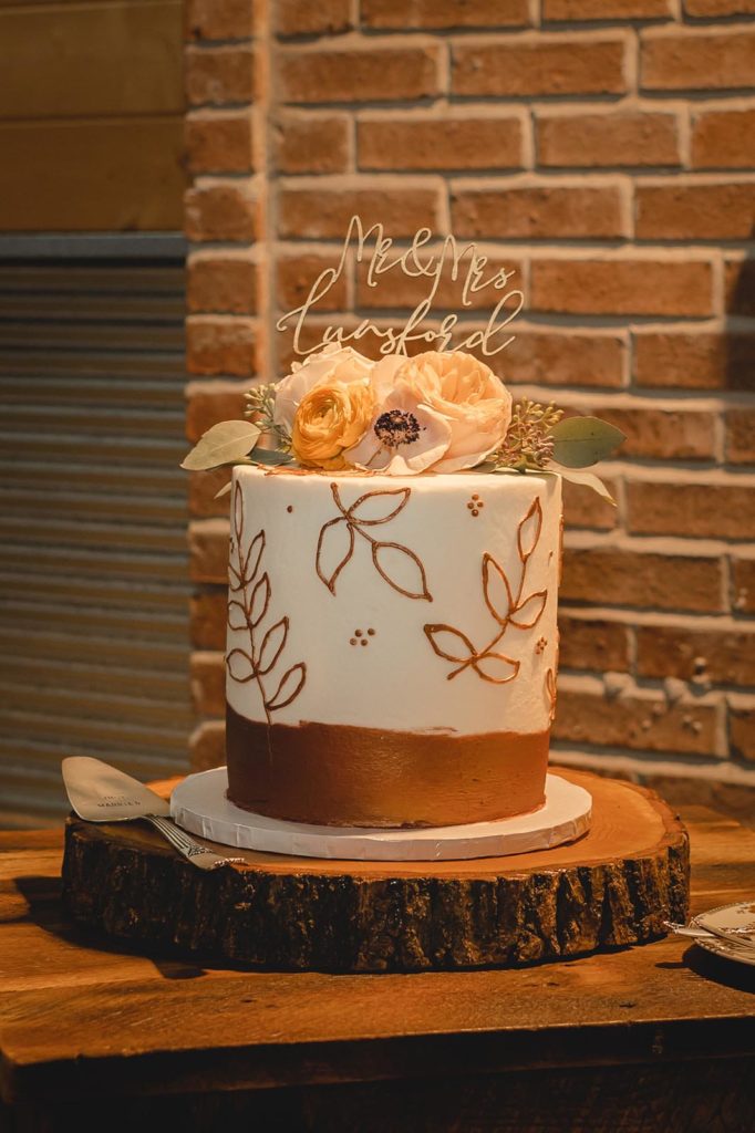 White and gold wedding cake with pink and orange flowers as well as green leafs