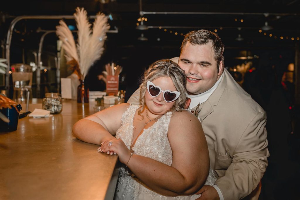 Sunglass wearing bride and groom pose at bar