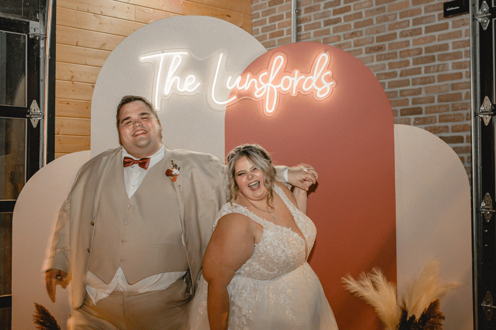 Bride and groom posing in front of neon side of wedding day.