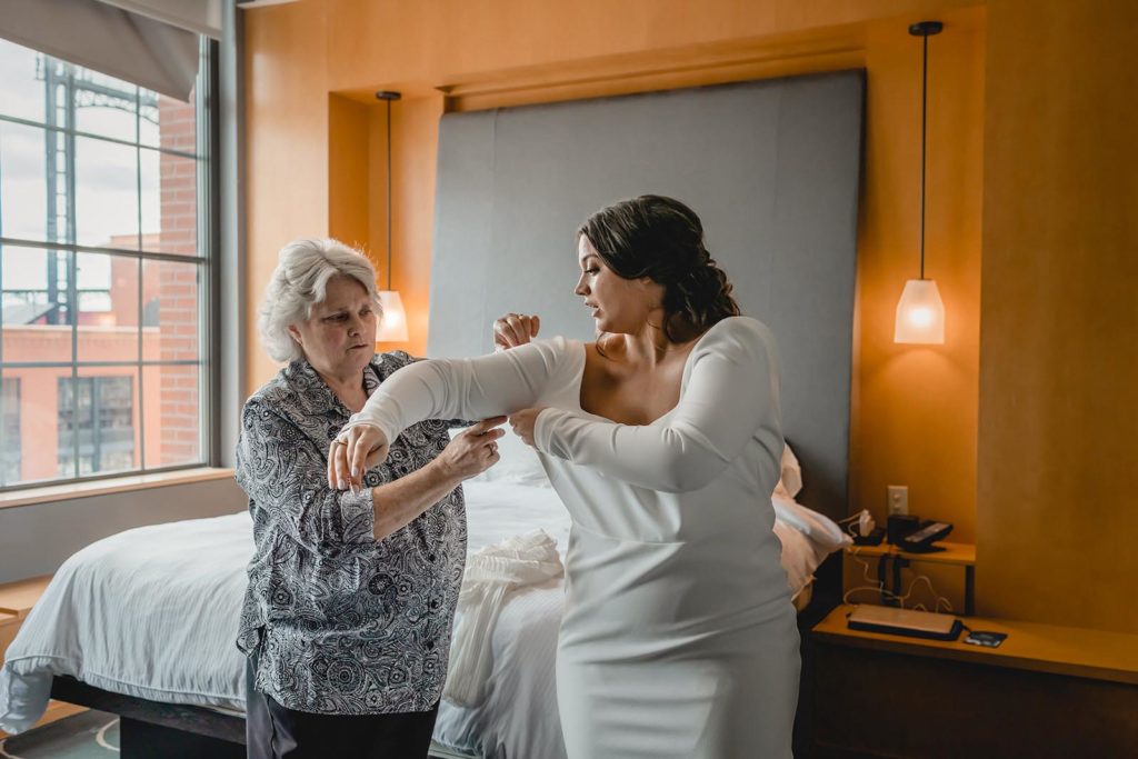 Mother helping bride put on wedding dress during her wedding day.