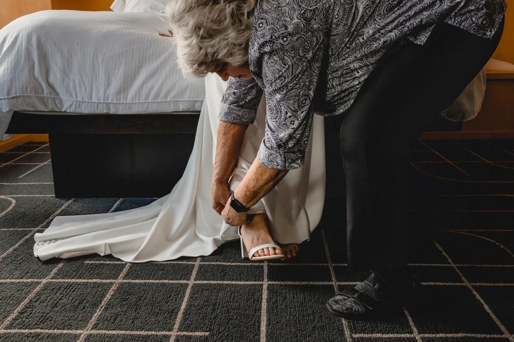 Mother of bride helping daugher put on her wedding shoes.