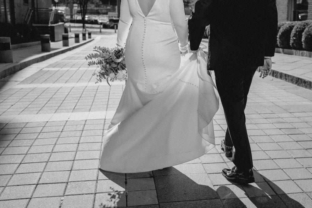 Black and white photo of bride and groom holding hands and walking