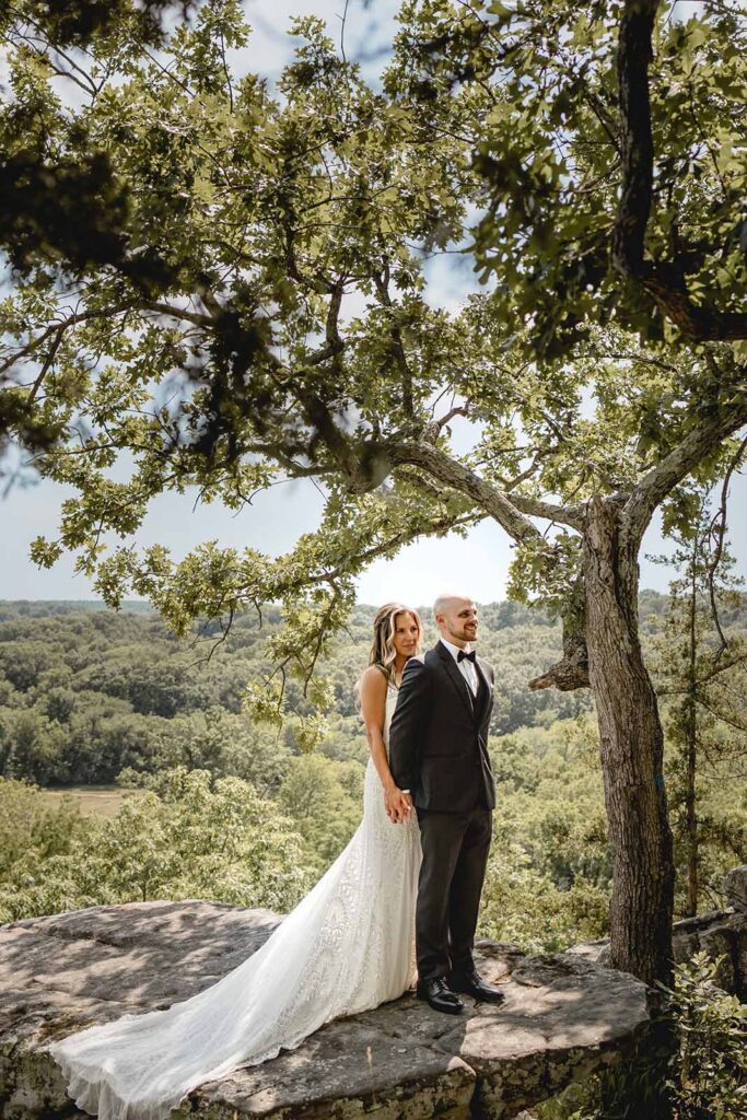 Bride and groom hold hands and look onward on top of a large rock perched at the edge of Lost Hill Lake's Thinking Rock scenic overlook