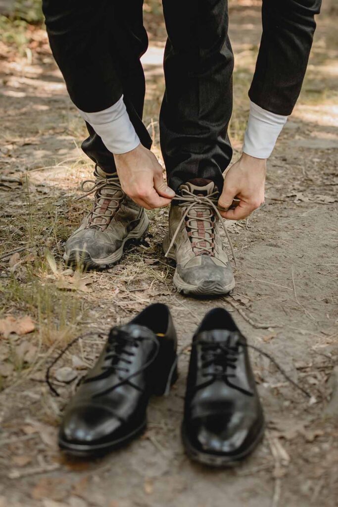Cropped shot of a groom tying his hiking shoes while his dress shoes lie out of focus in the foreground