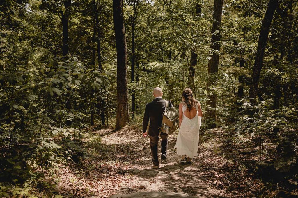 Shot of the back of a bride and groom as they descend a hike in the woods at Lost Hill Lake