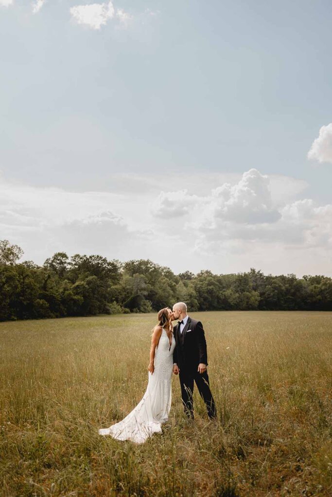 Full body shot of bride and groom leaning in for a kiss centered in a summer field