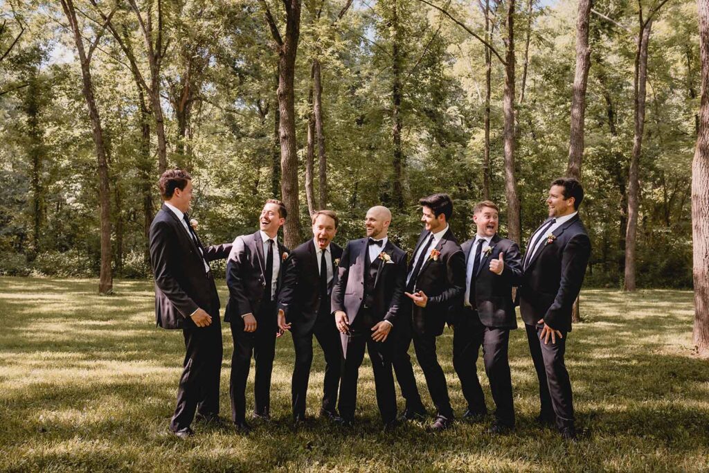 Groom centered among his 6 groomsmen as they all candidly laugh together