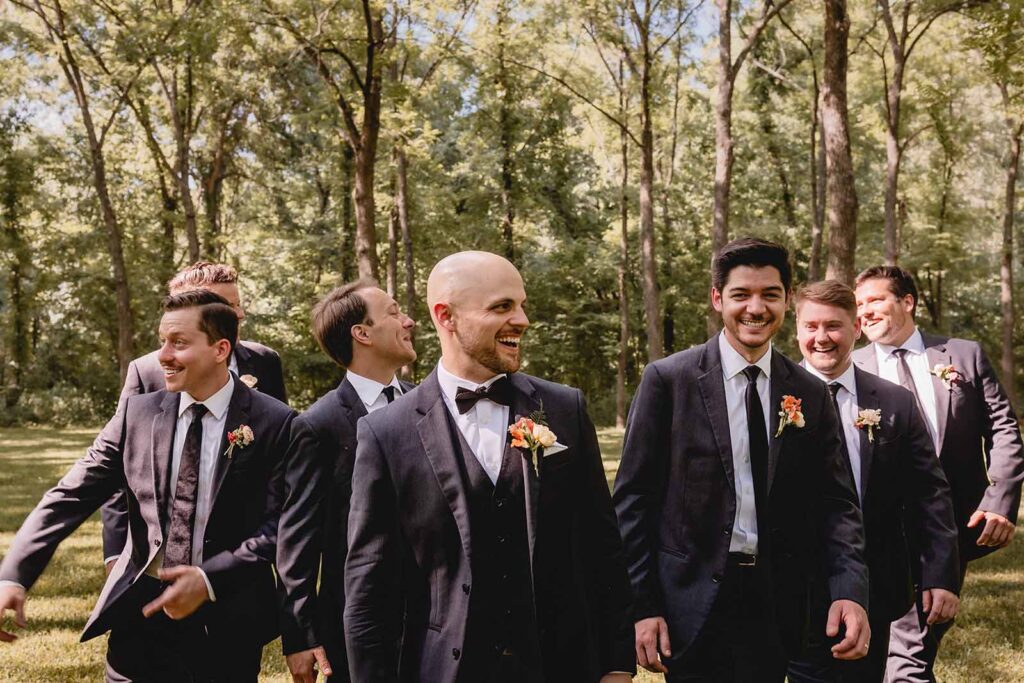 Groom laughs to his bride off camera walking as his grooms men flank behind