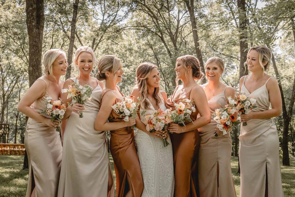 Closeup of centered bride surrounded by her 6 bridesmaids candidly laughing with their bouquets