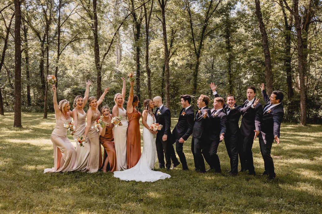 Bride and groom kiss in the center as their wedding party cheers on either side 