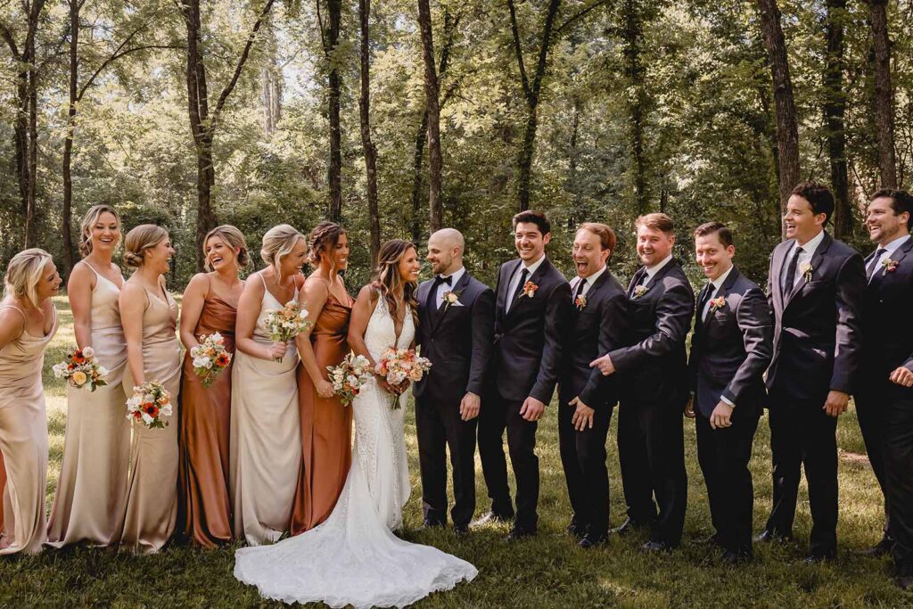 Bride and groom look happily towards each other in the center as bridesmaids and grooms flank them on both sides
