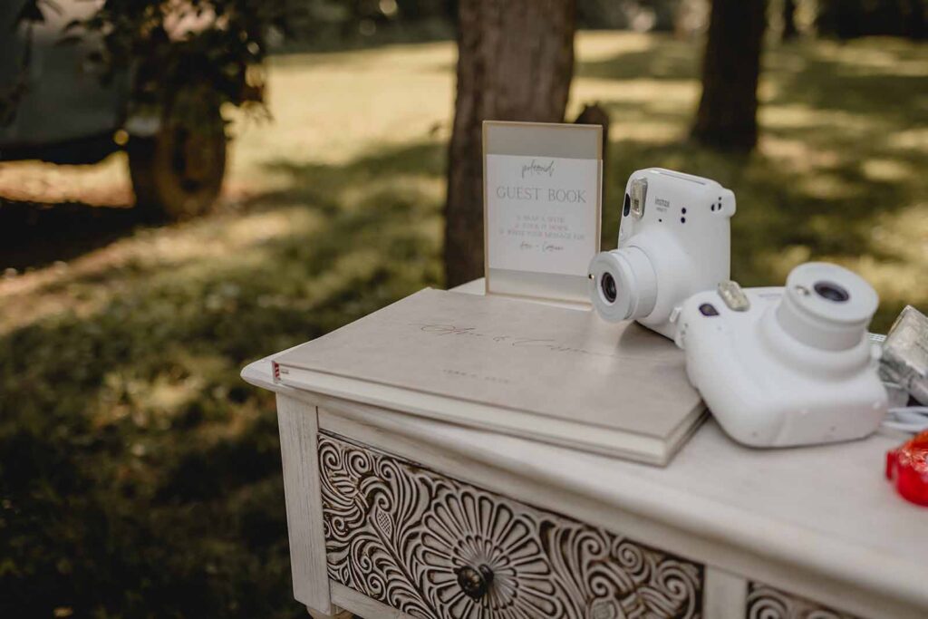 Two instax film cameras lay on a leather wedding guest book on antique white wooden table