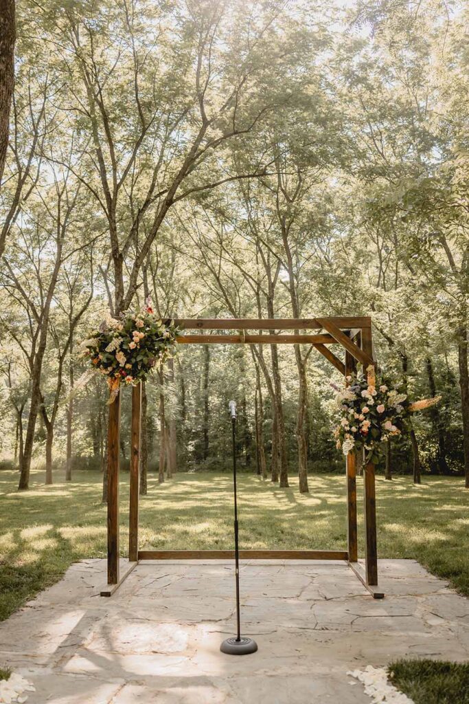 A microphone stand sits centered in between a wooden rectangular arbor with 2 oversized floral bouquets pinned on either side