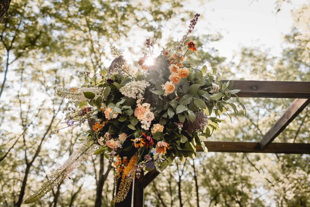 Close up of arbor floral arrangement with greenery, peach, orange white and pink wildflowers