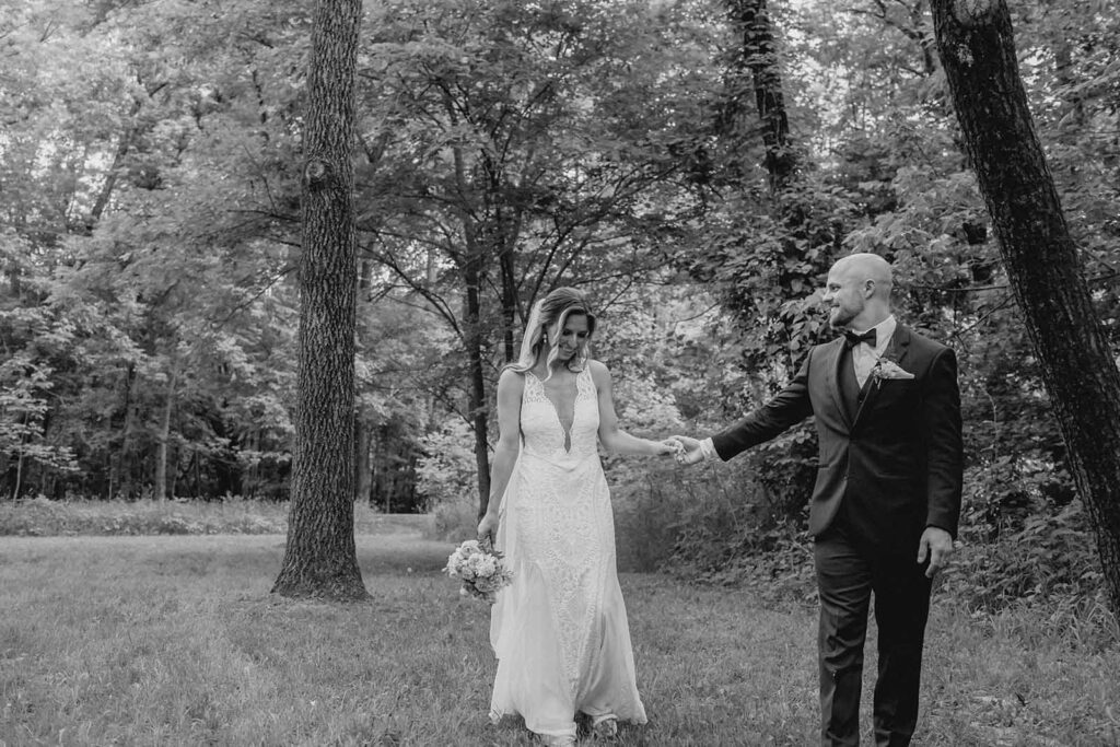 black and white shot of bride and groom giggling as they hold hands and walk for newlywed photos outside