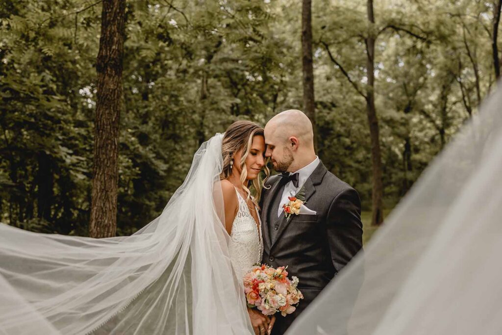 Bride and groom rest foreheads together as long veil artfully surrounds them on both side of the frame