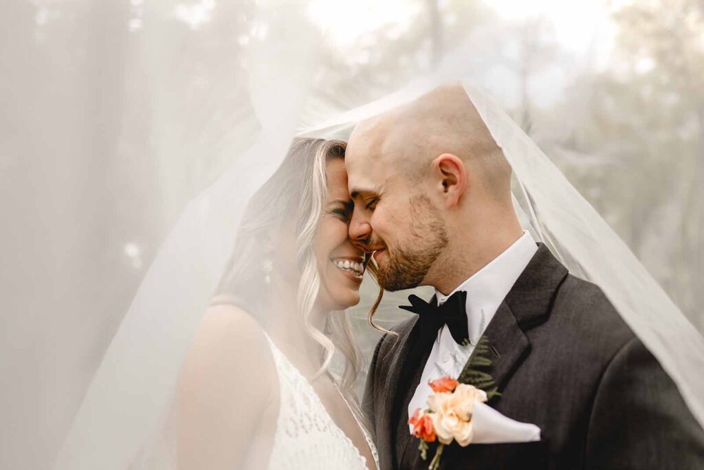 Close up of bride and groom giggling close together under a long veil