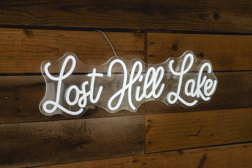 Neon script sign mounted on a wooden wall reads "Lost Hill Lake"
