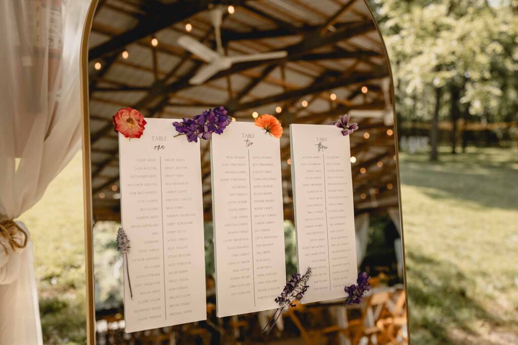 Close up of table seating chart comprised of 3 pages afixed to a standing mirror with dried wildflowers