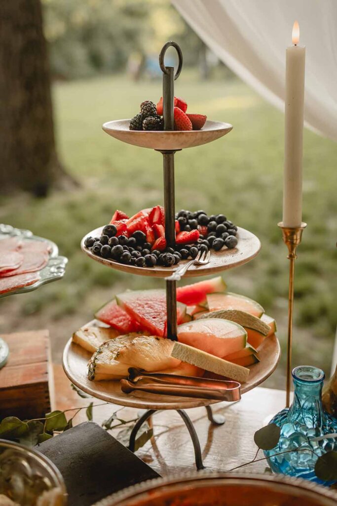 Closeup of an antique 3 tiered serving stand with fresh berries, pineapple and watermelon in an eclectic table setting