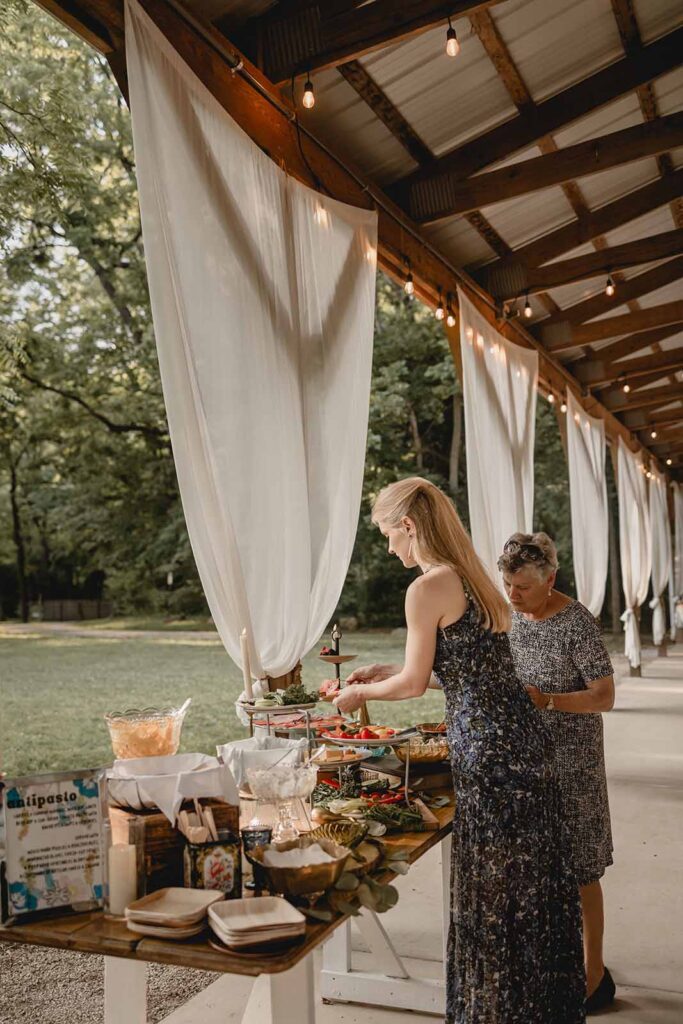 Guests fill their plat at an outdoor anitpasto bar under a wooden pavilion lined with white curtains