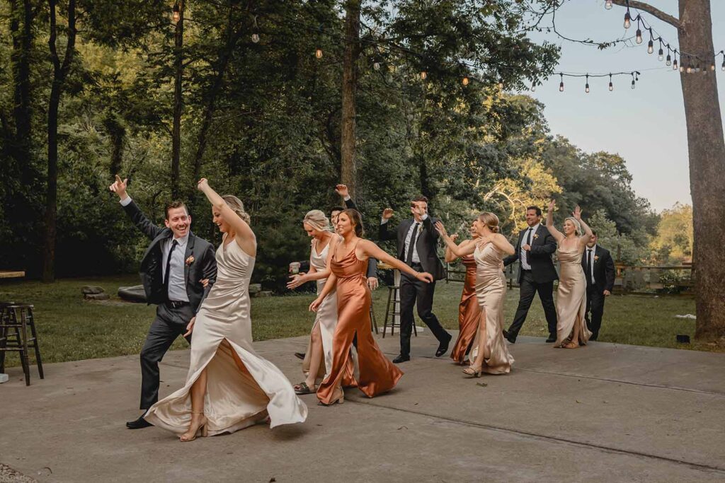 Wedding party enthusiastically cheers and dances across the concrete outdoor dancefloor into the reception