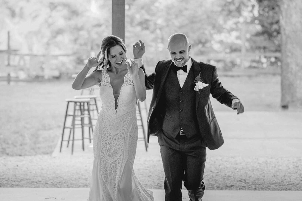 Black and white shot of bride and groom dancing their way into reception outside