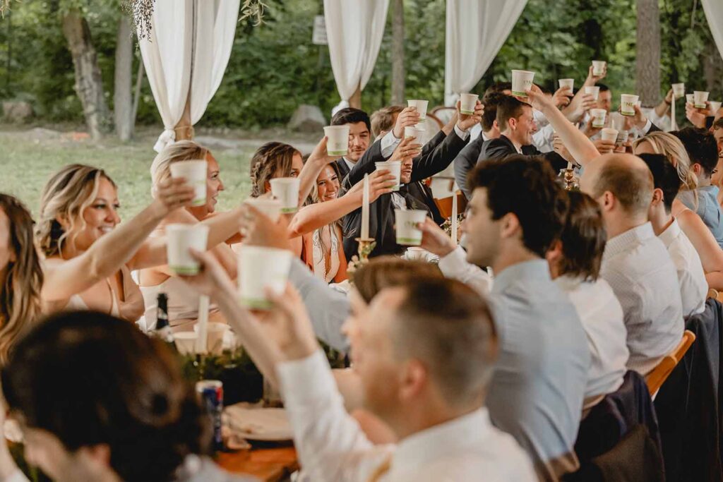 Head table of wedding party raise biodegradable cups to cheers after wedding toast