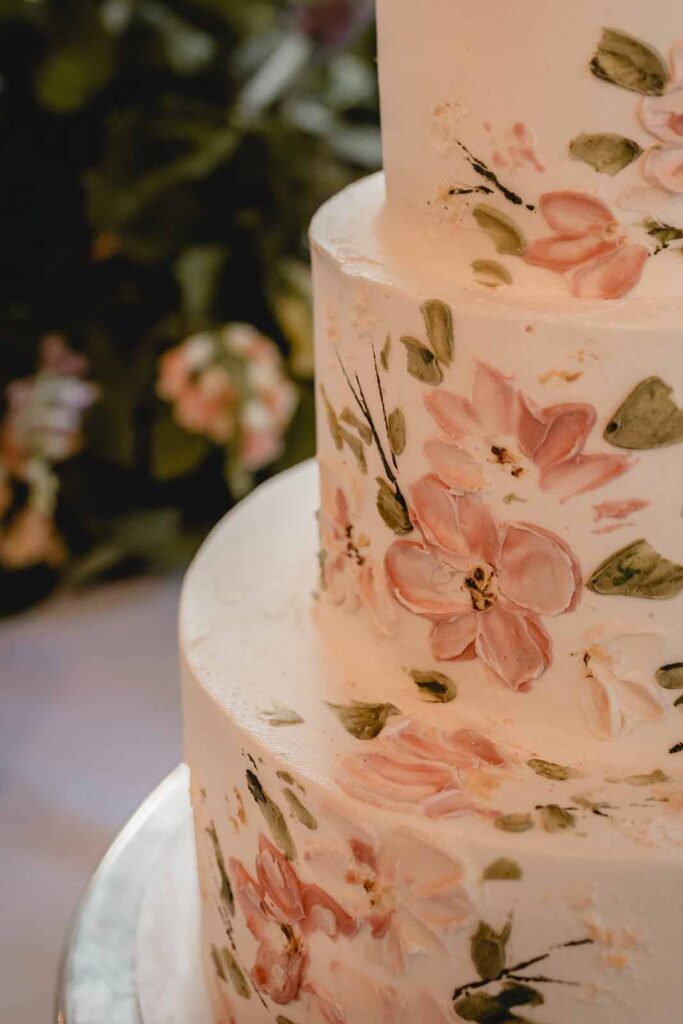 Close up of painted pink and green wildflower design on three tier white wedding cake