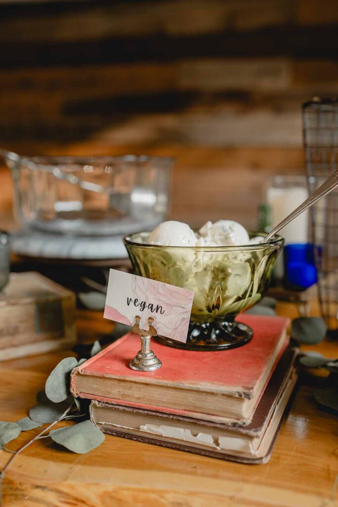 Close up of a green serving dish with scoops of vegan butter on top of a stack of vintage books in eclectic dinner buffet setup