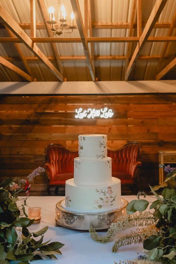 Three tier white wedding cake sits on white dessert table in cozy wooden alcove