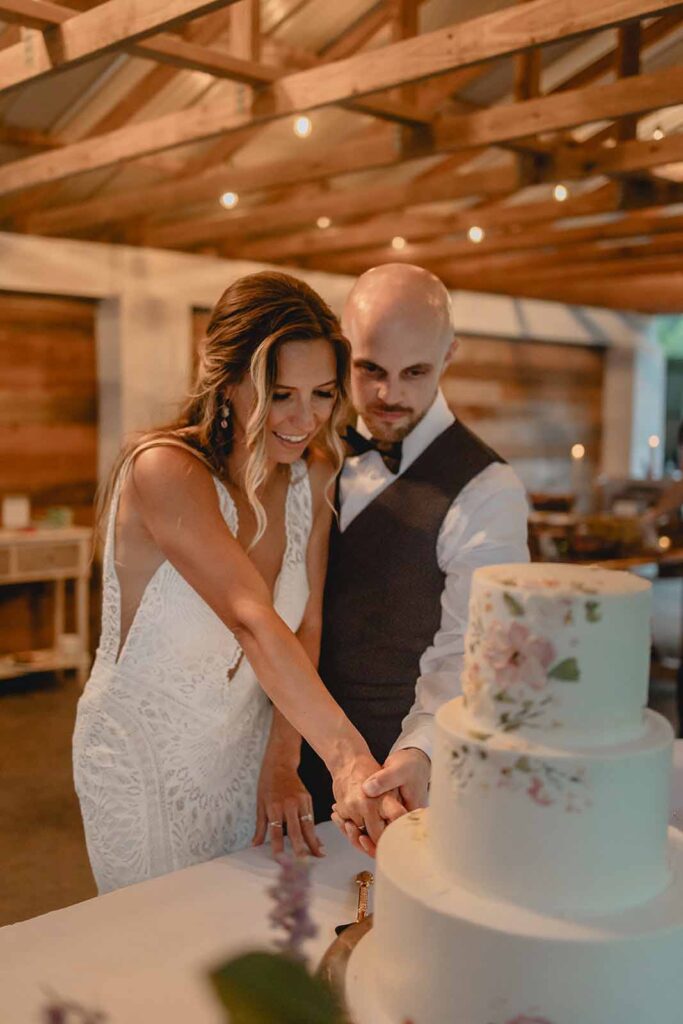 Bride and groom holding knife together to cut their three tier white wedding cake