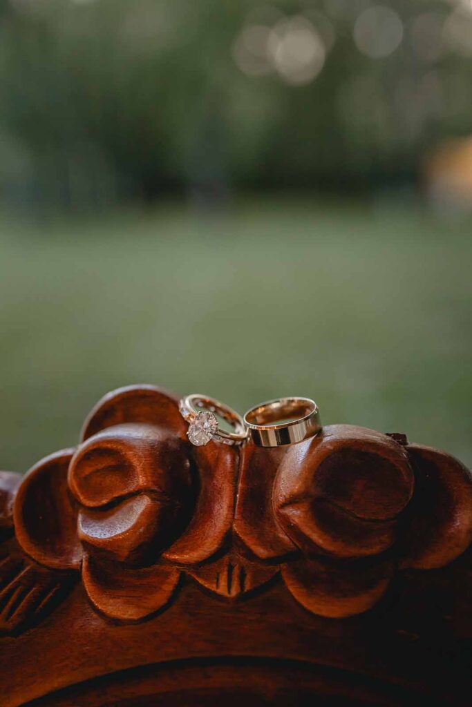 Close up of gold wedding rings perched on top of ornate wood carved floral furniture frame