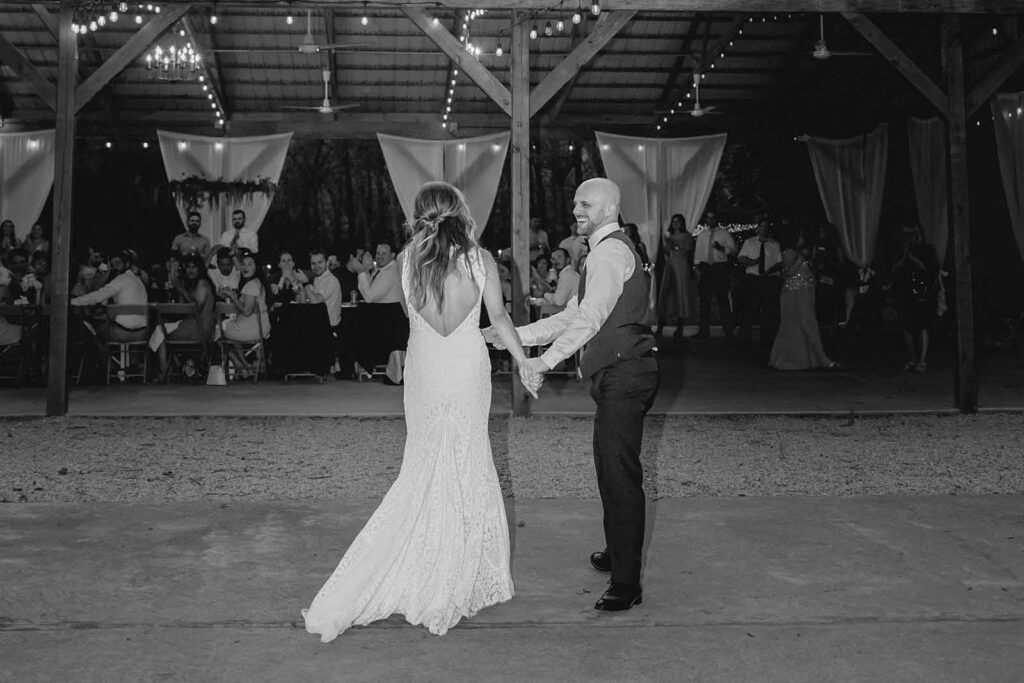 Black and white shot of bride and groom laughing and walking off the dancefloor