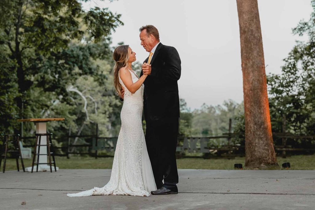 Bride and her father holding hands and swaying during their first dance outside during blue hour