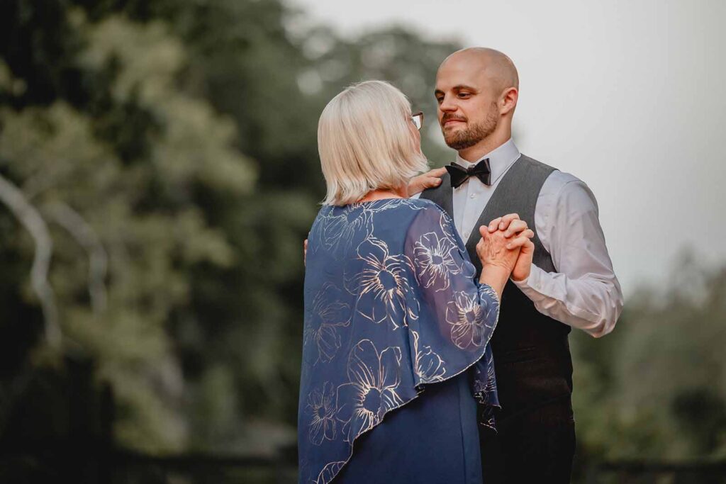 Groom and his mother holding hands and swaying during their first dance outside during blue hour