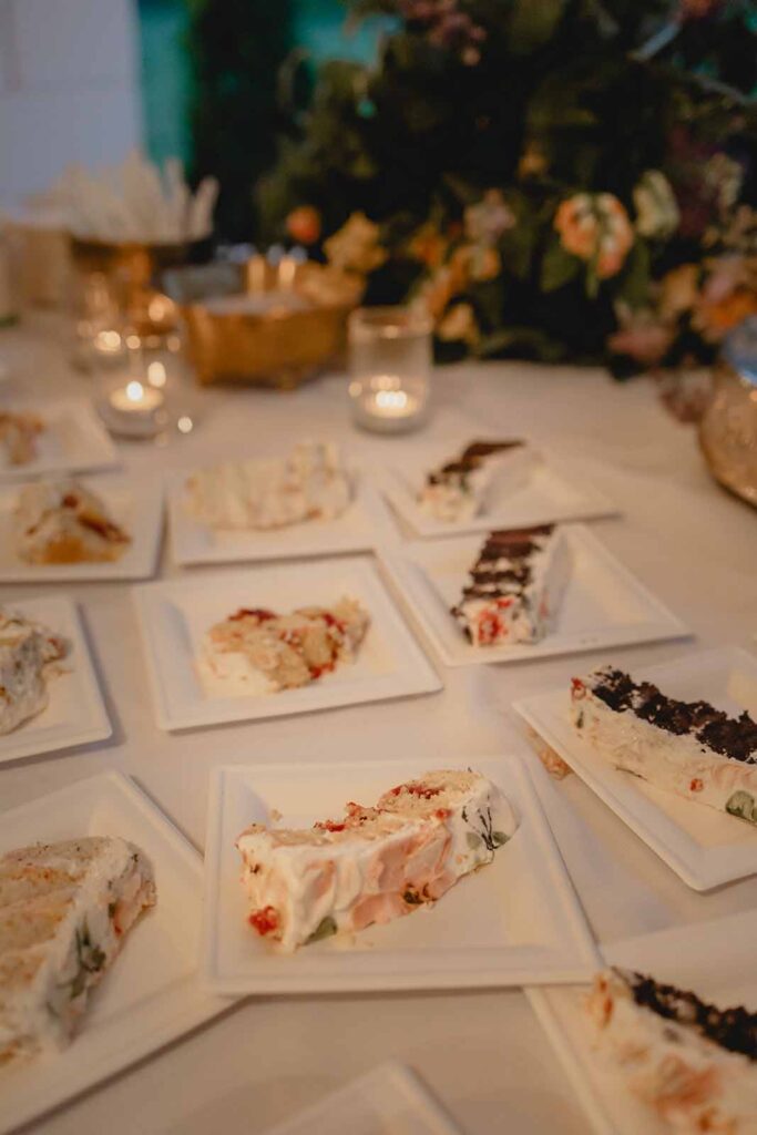 Slices of cake on white square plates span the white dessert table