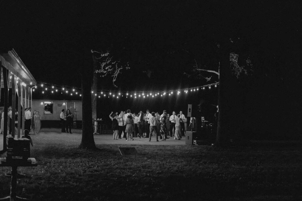 Black and white wide shot of Lost Hill Lake dance floor filled with wedding guests under the string lights